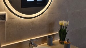 Un bagno con uno specchio rotondo, un lavabo e un vaso di tulipani bianchi.