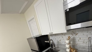 Een compacte keuken met witte kastjes, een roestvrijstalen magnetron en een zwarte oven.