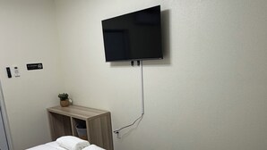 Een hotelkamer met een bed, een aan de muur bevestigde televisie, een klein houten kastje en een 'Niet roken'-bord.