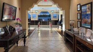 A hotel lobby with a reception desk, a large screen displaying a Valentine's Day ad, and framed awards on the walls. - Disney Resort Escape w/ Pirate Pool & Spa Sleep 6 (Orlando)
