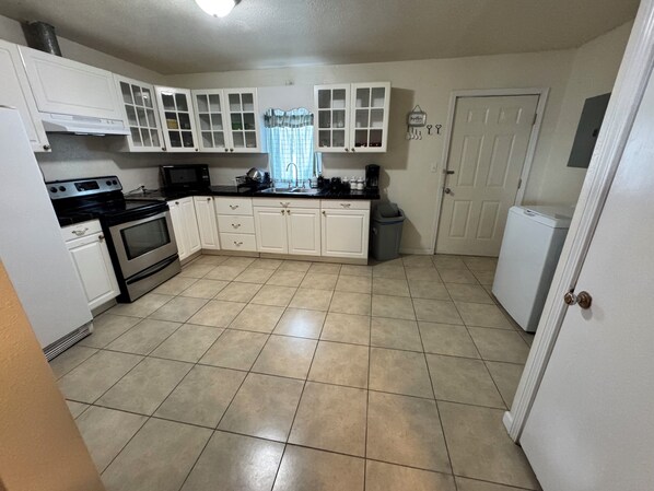 A kitchen with white cabinets, a stove, an oven, a microwave, and a refrigerator.