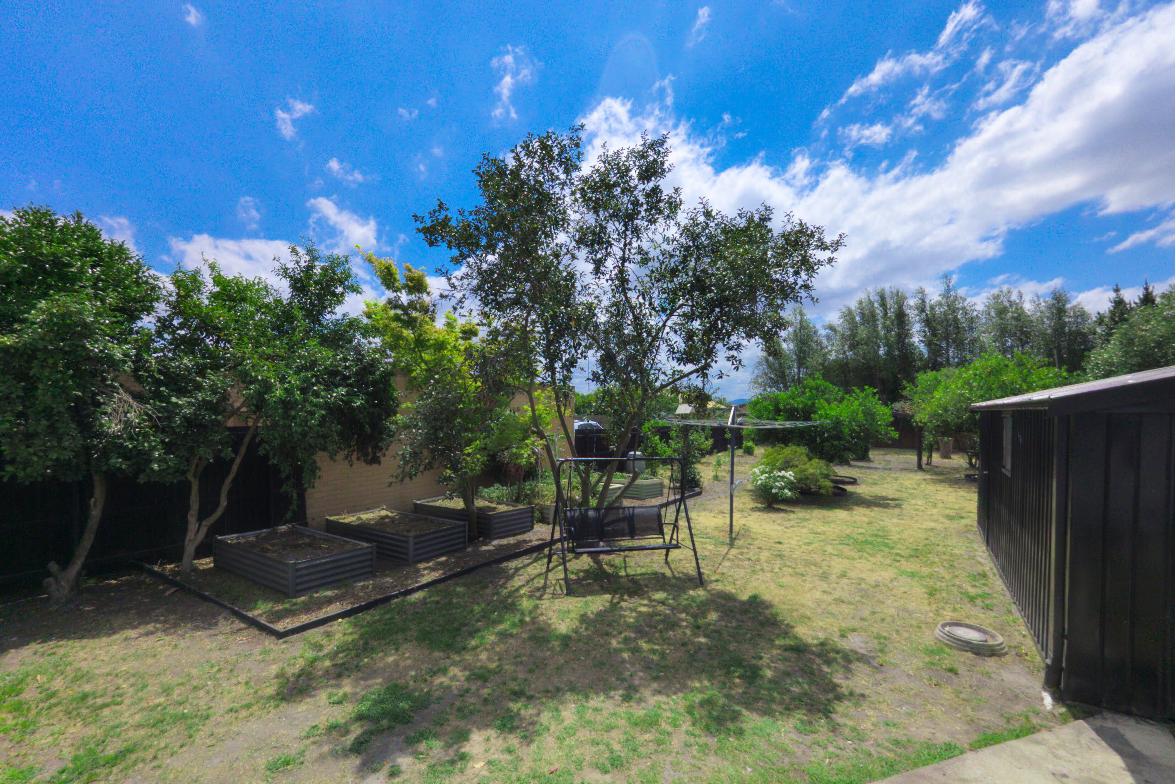 A backyard with a swing set, a small shed, and a garden area.