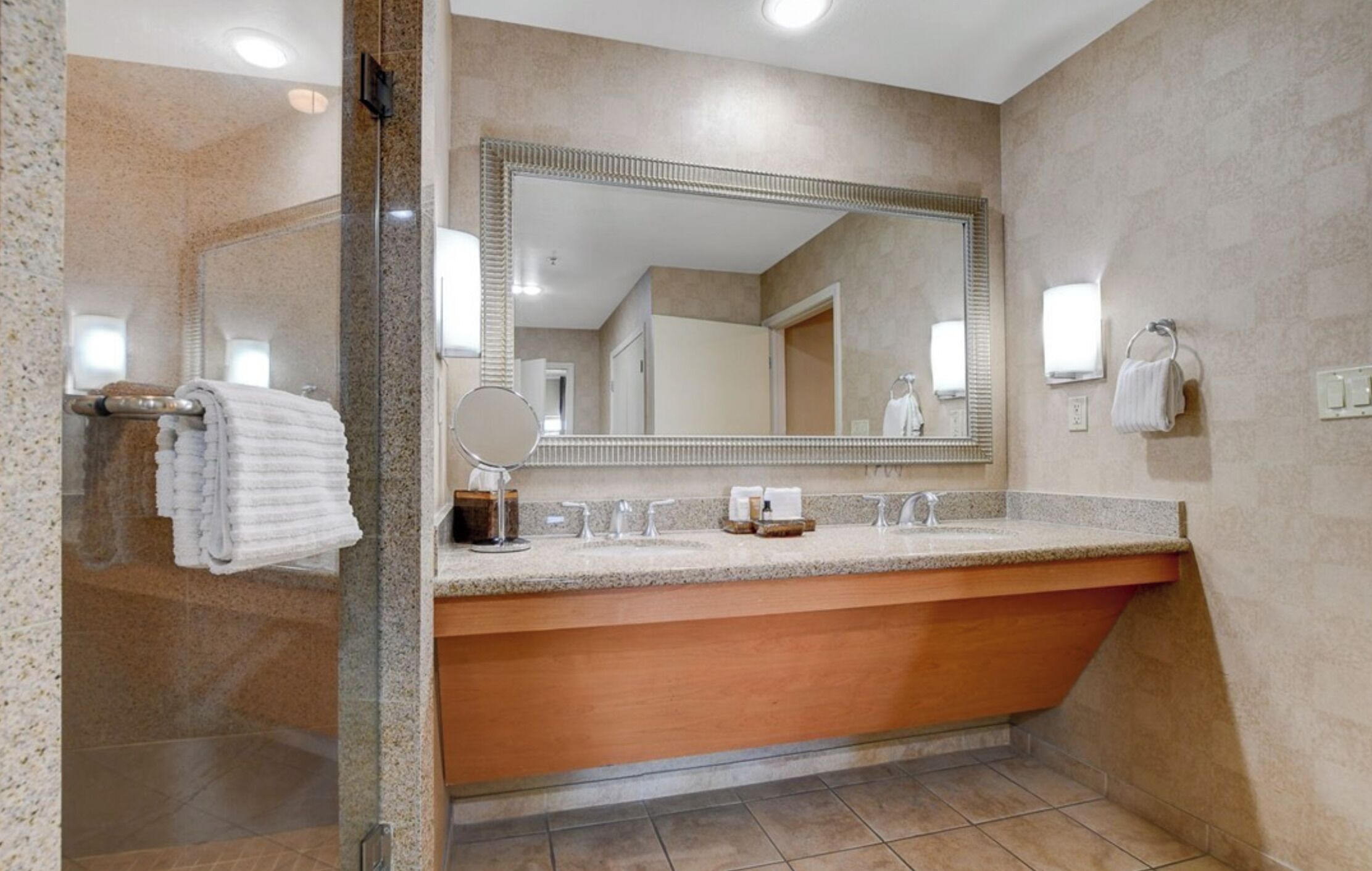 A bathroom with a large mirror, a sink with a countertop, a shower area, and towels hanging on a rack.