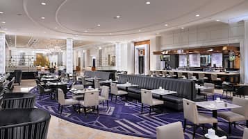 A spacious hotel lobby with multiple seating areas, a bar, and a reception desk.