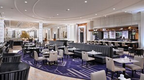 Un hall d’hôtel spacieux, doté de plusieurs espaces salon, d’un bar et d’un comptoir d’accueil.