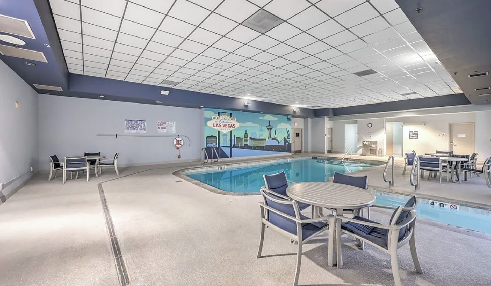 Un espace piscine agrémenté d’une fresque murale, de chaises longues et de tables.