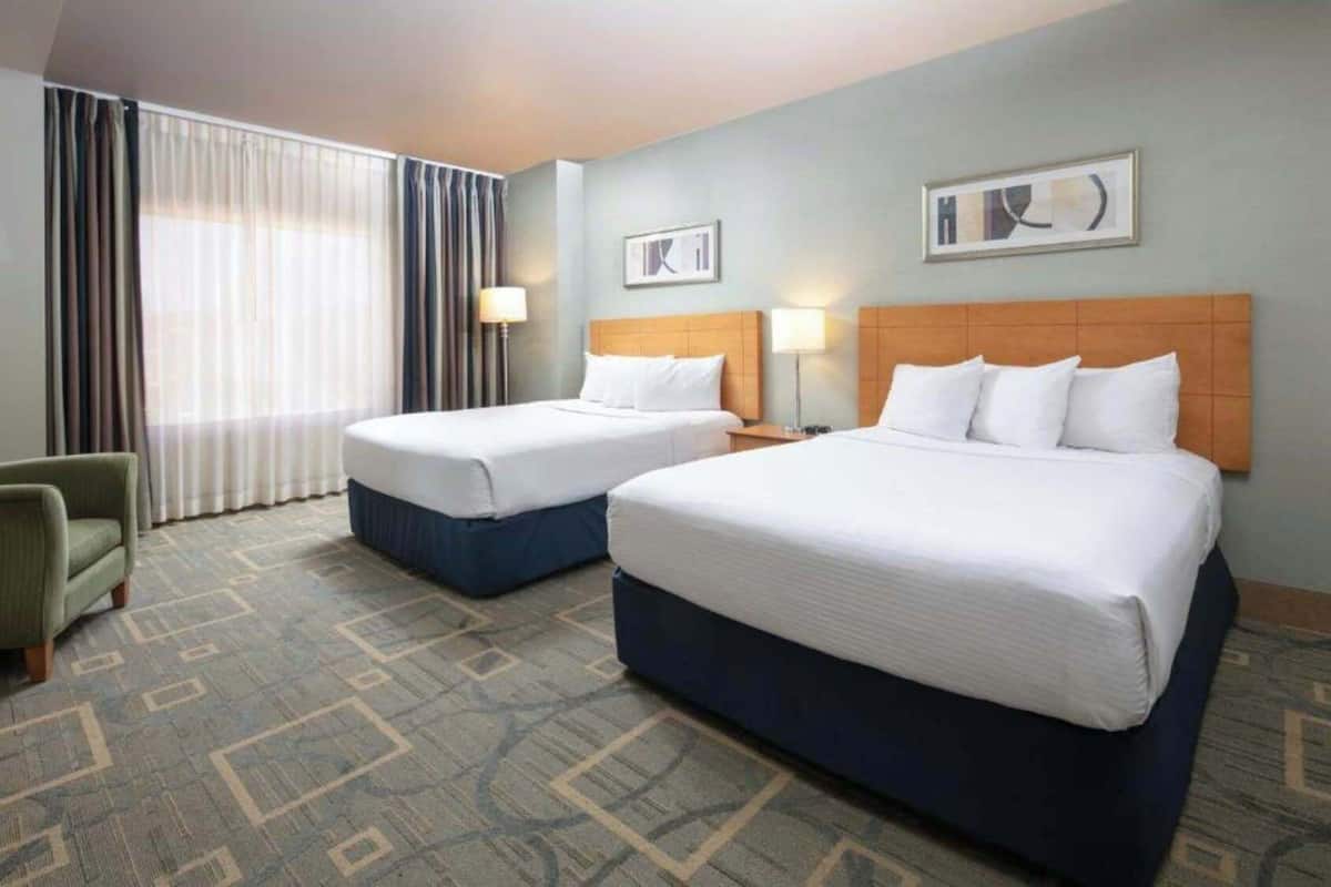 A hotel room with two beds, a chair, and a large window with curtains.
