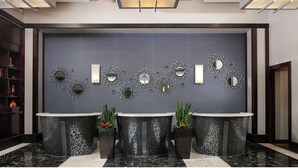 Un espace d’accueil avec un mur de couleur sombre, des miroirs décoratifs et trois présentoirs pour plantes.