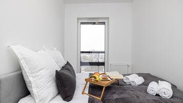 Hotellihuone, jossa on sänky, tyynyjä, hedelmiä sisältävä tarjotinalusta ja kirja sekä ikkuna, josta on näkymä.