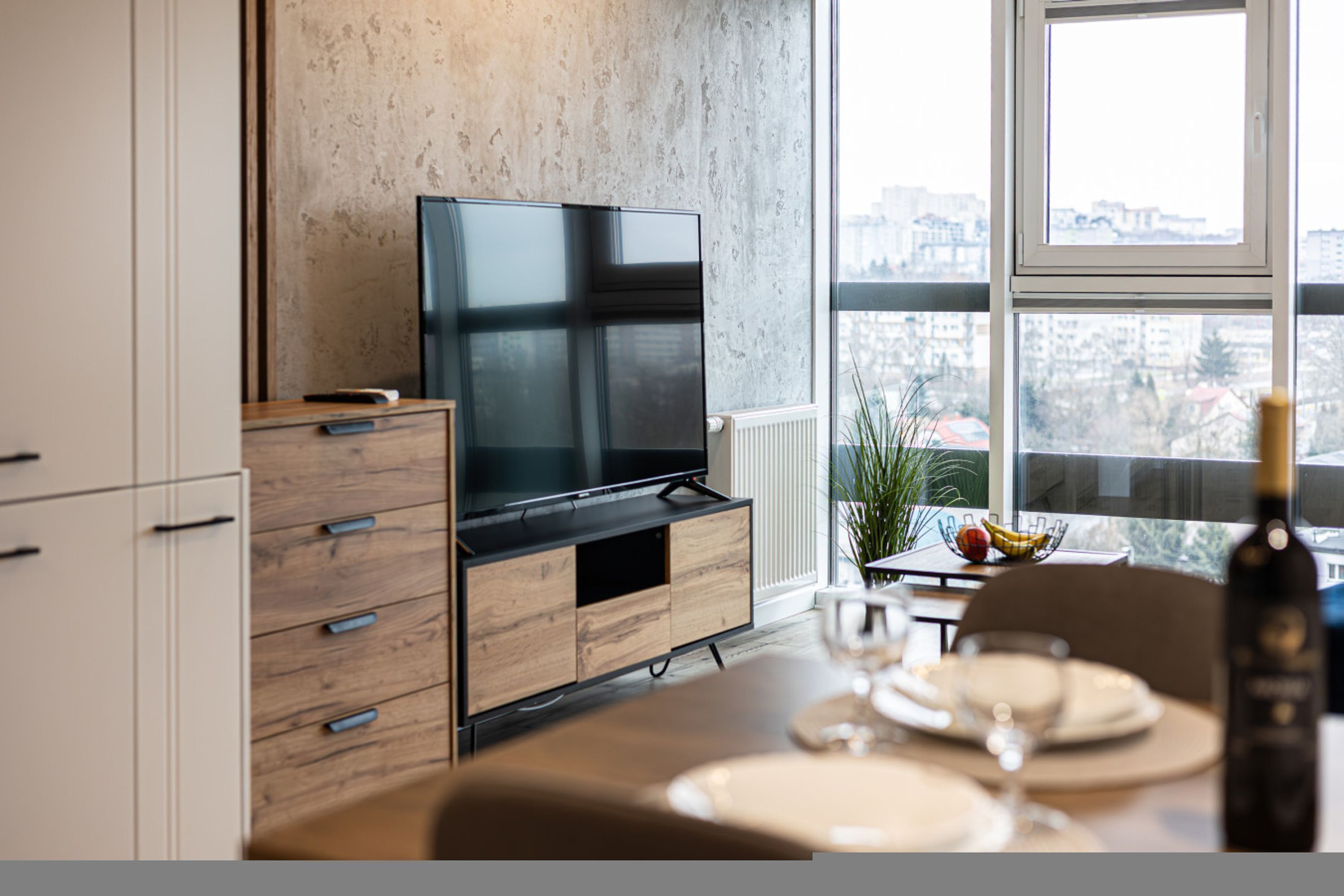 A modern kitchen with a built-in TV, wooden cabinetry, and a dining area with a table set for two.