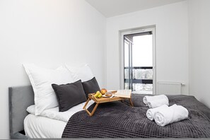 Ein modernes Schlafzimmer mit Bett, Kissen, einem Tablett mit Früchten und einem Buch sowie einem Blick ins Freie durch ein Fenster.