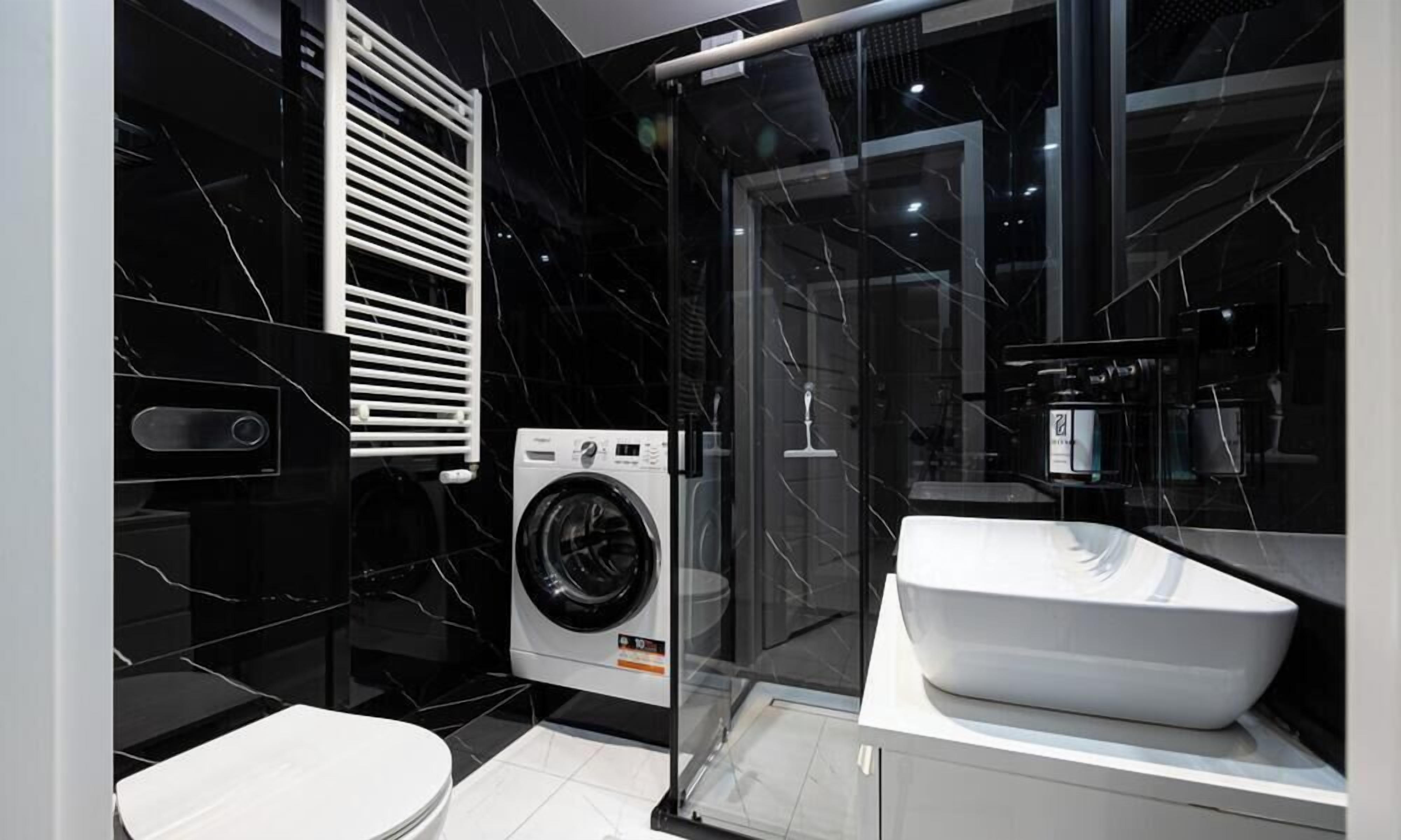 A modern bathroom with a black marble wall, a white sink, and a built-in washing machine.