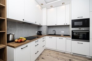 Una cocina moderna con armarios blancos, encimera negra, hervidor de acero inoxidable y una cesta de fruta.