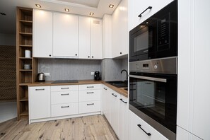 A modern kitchen with white cabinetry, a wooden countertop, and built-in appliances including a microwave and oven.