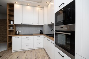 Una cocina moderna con armarios blancos, encimera de madera y electrodomésticos integrados, incluyendo un microondas y un horno.