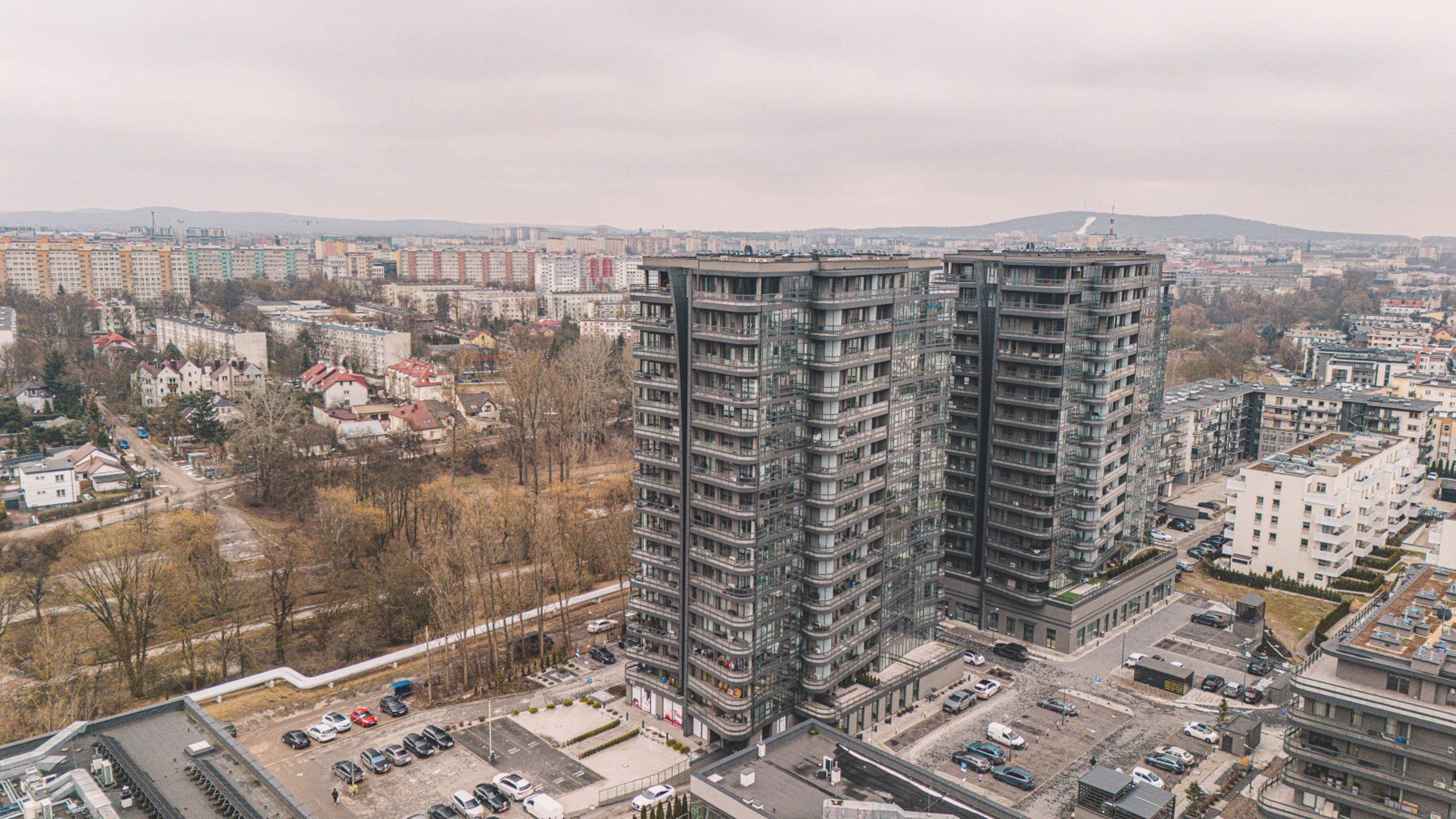 Een hoog appartementencomplex met meerdere balkons, omringd door andere gebouwen en een parkeerplaats.