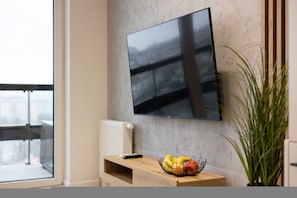 Una sala de estar moderna con un televisor de pantalla plana montado en la pared, una mesita de madera con un frutero y una planta en maceta.