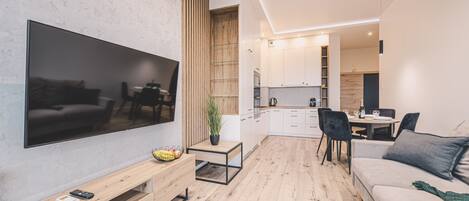 Un salon moderne doté d’un téléviseur à écran plat, d’une table basse en bois, d’un canapé et d’un coin repas avec une table et des chaises.