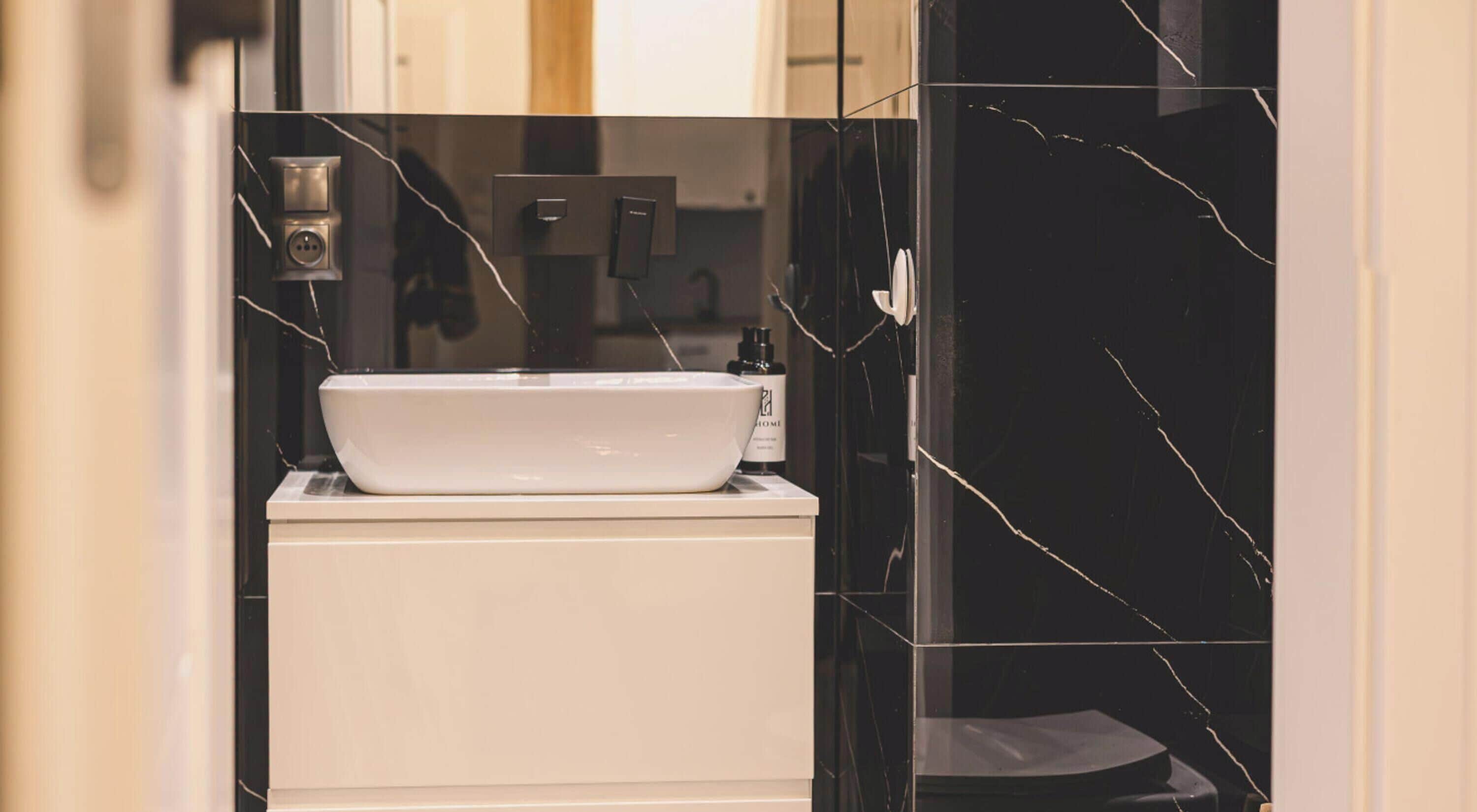A bathroom with a white sink, black marble walls, and a white toilet.