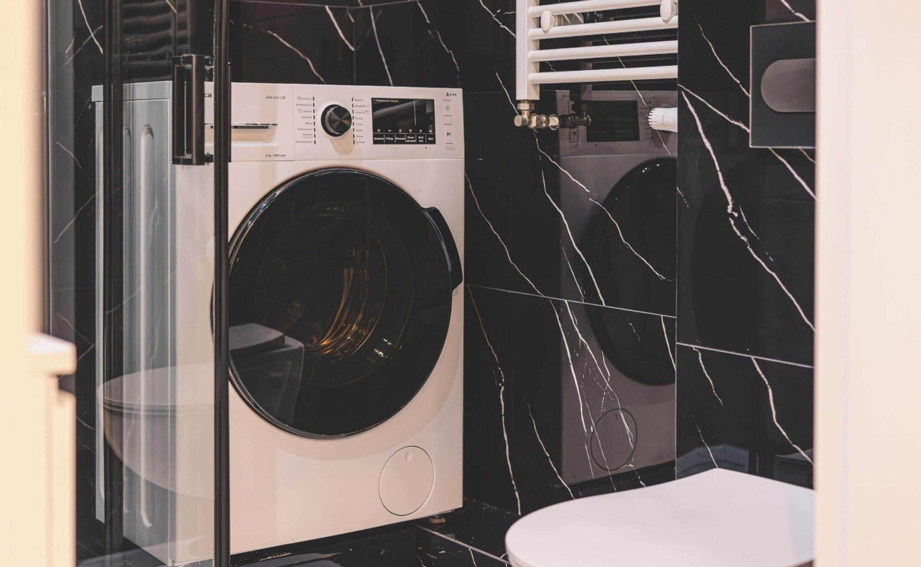 Een moderne wasruimte met een voorlader wasmachine en een droger, met een zwarte marmeren wand met witte aders.