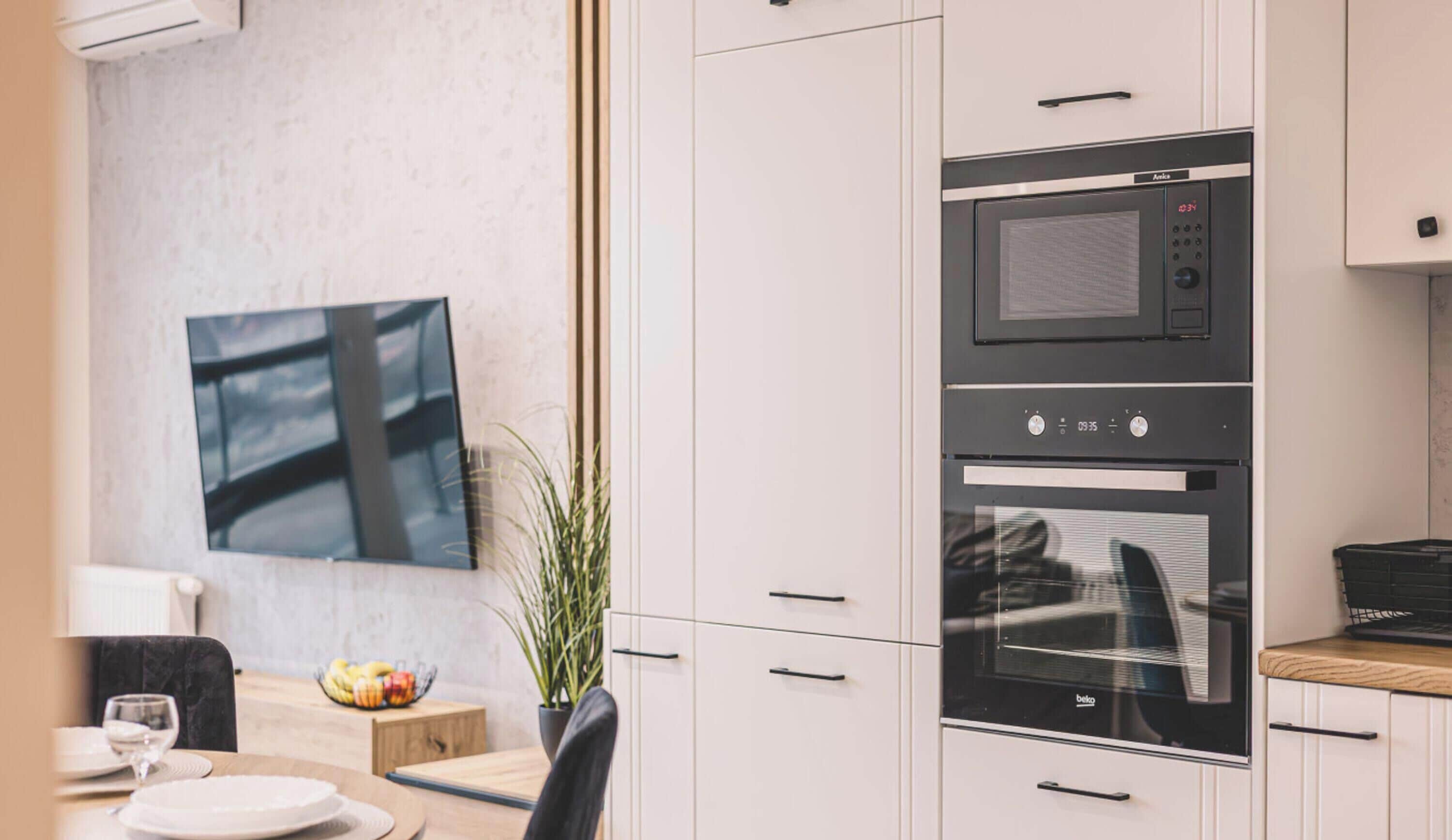 A modern kitchen with a built-in microwave and oven, a dining area with a table and chairs, and a potted plant.