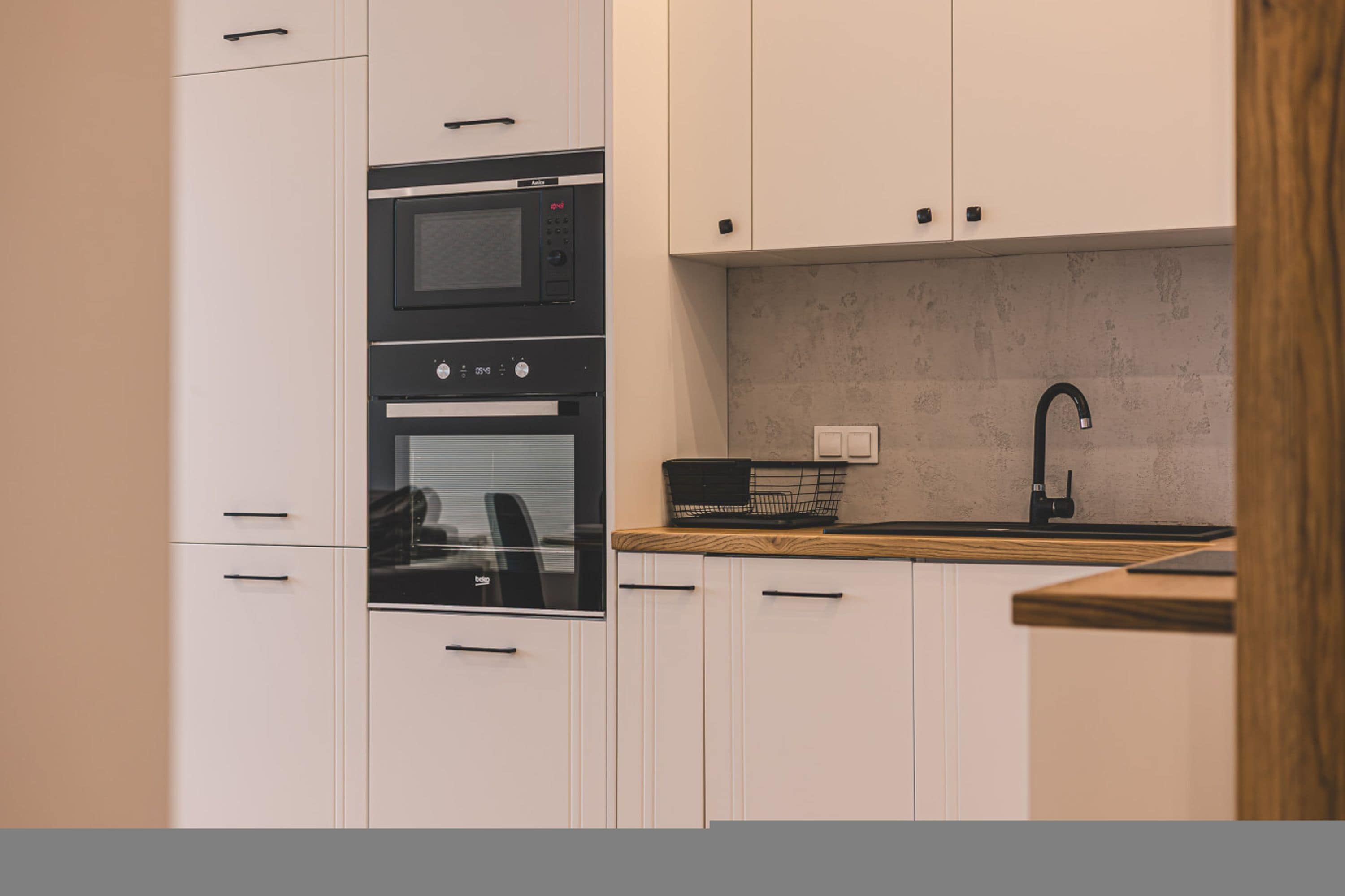 A modern kitchen with white cabinetry, a built-in oven, a microwave, and a sink with a faucet.