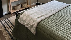 Een slaapkamer met een bed, een nachtkastje met manden, een vloerlamp, een schilderij en een raam met uitzicht op bomen.