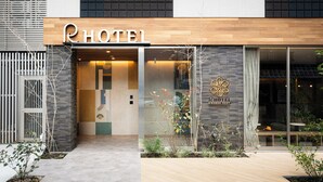 A modern hotel entrance with a wooden facade, glass doors, and a visible logo. - R Hotel Namba East (Osaka)