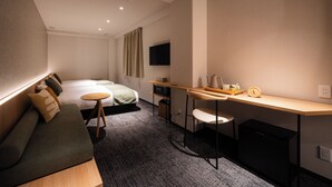 A modern hotel room with a sofa, a bed, a desk with a chair, a television, and a coffee maker. - R Hotel Namba East (Osaka)