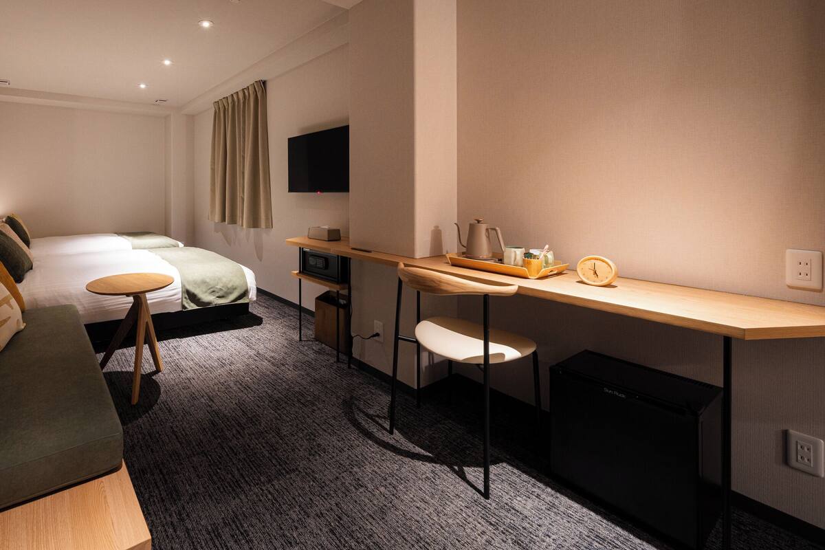 A modern hotel room with a sofa, a bed, a desk with a chair, a television, and a coffee maker.