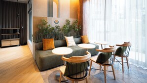 A modern living area with a sofa, round tables, and chairs, a wooden cabinet, and a large window with sheer curtains. - R Hotel Namba East (Osaka)