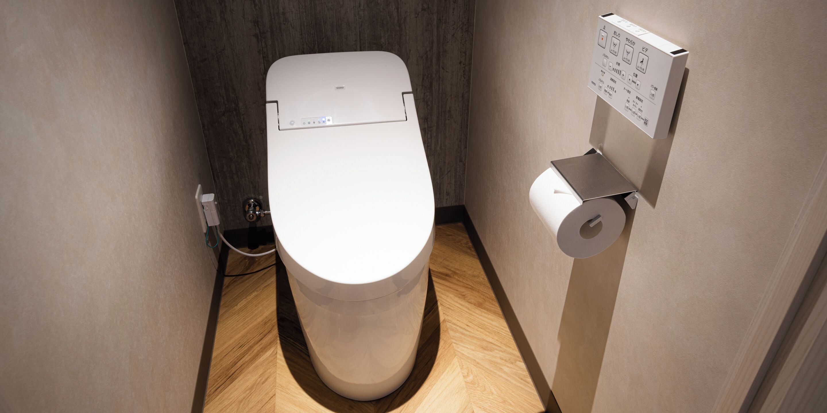 A modern, compact toilet with a control panel, a toilet paper holder, and a visible plumbing connection.