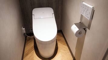 A modern, compact toilet with a control panel, a toilet paper holder, and a visible plumbing connection.