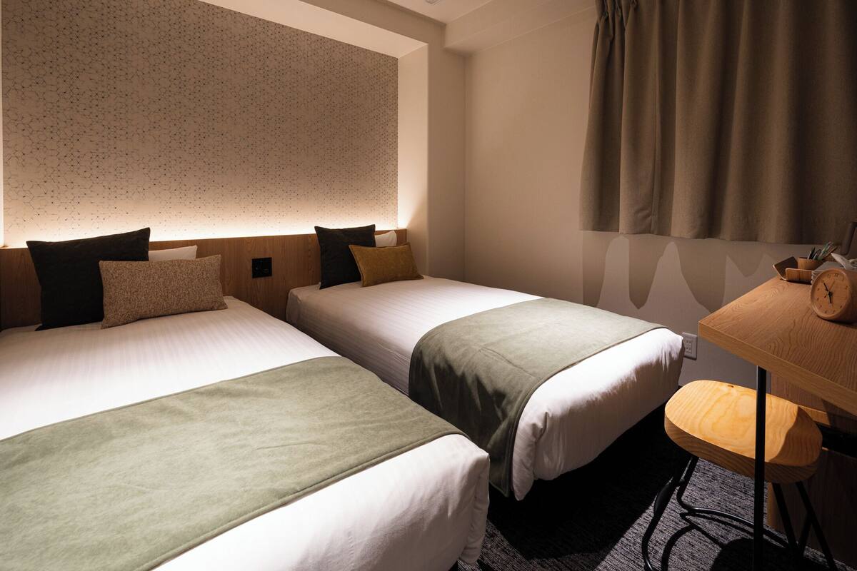 A hotel room with two beds, a desk, and a chair.