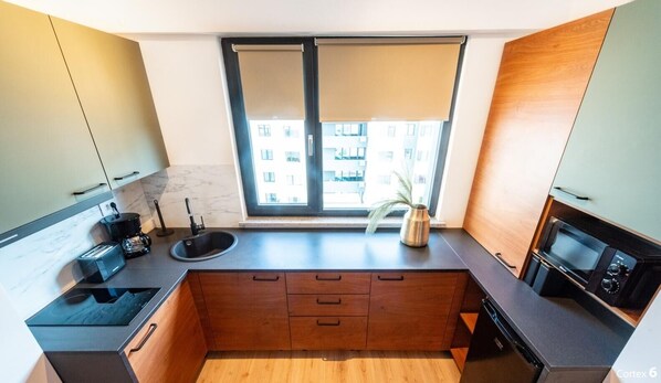 A modern kitchen with a built-in oven, a sink, and a window with a view of buildings. - Color Ivory Residence with Free Parking (Voluntari)