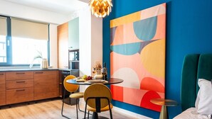 Eine moderne Küche mit Holzausbau, einem Esstisch mit gelben Stühlen und einem farbenfrohen, abstrakten Gemälde an der Wand.