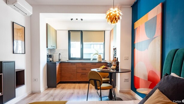 Eine moderne Küche mit Holzschränken, einem Esstisch mit Stühlen und einem farbenfrohen, abstrakten Gemälde an der Wand.