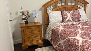 A bedroom with a wooden bed, a nightstand with drawers, a lamp, and a potted plant. - Adorable 4-bedroom house with AC in charming Attleboro (Attleboro)