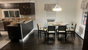 A modern kitchen with dark wooden cabinets, a central island, and a dining area with a glass table and chairs. - Adorable 4-bedroom house with AC in charming Attleboro (Attleboro)