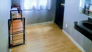 Een kamer met een houten vloer, een zwarte mat, een kledingrek, een deur en een spiegel.