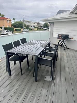 Eine Terrasse mit Holztisch und -stühlen, einem Grill und Blick auf die Nachbarschaft.