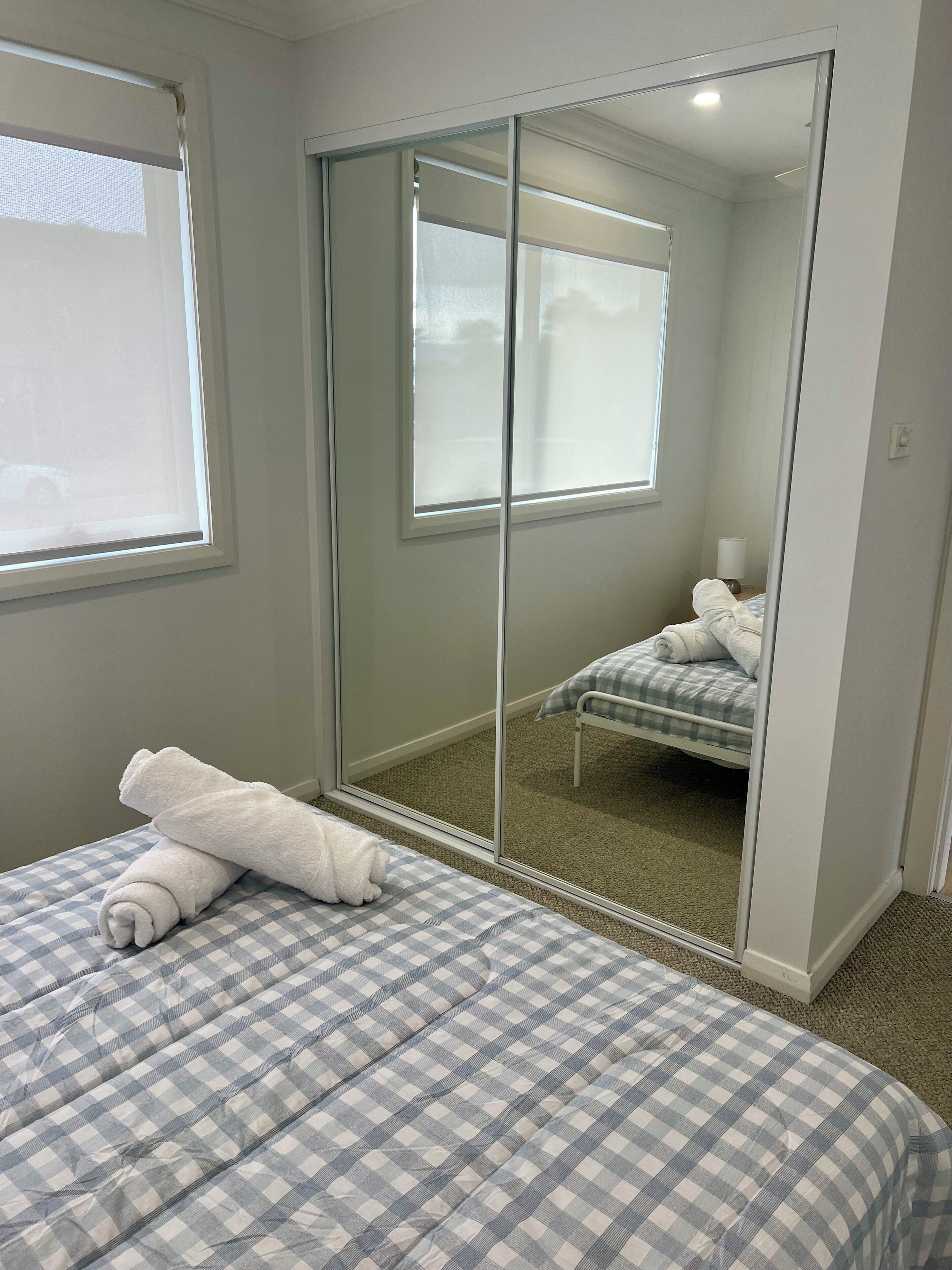 A bedroom with a checkered bedspread, a large mirror, and a view of a bed with a pillow and blanket.