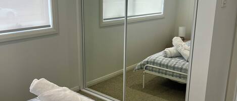 A bedroom with a checkered bedspread, a large mirror, and a view of a bed with a pillow and blanket.