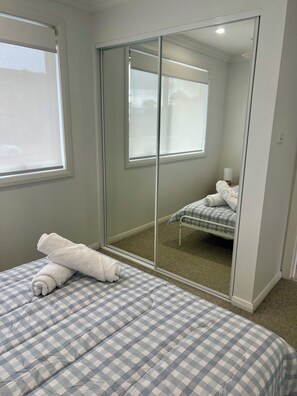 Ein Schlafzimmer mit karierter Bettdecke, einem großen Spiegel und Blick auf ein Bett mit Kopfkissen und Decke.
