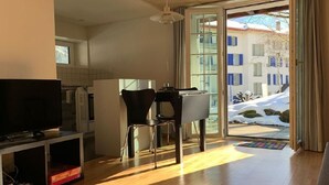 Moderni olohuone, jossa on televisio, ruokailutila tuoleineen sekä suuri liukuovi, joka johtaa lumiselle ulkoalueelle.