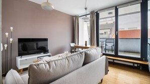 Un salon moderne doté d’un téléviseur à écran plat, d’un canapé, d’une table à manger et d’une grande fenêtre offrant une vue sur la ville.