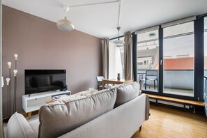 A modern living room with a flat-screen TV, a sofa, a dining table, and a large window offering a view of the city. - Blueground | Landstraße, balcony, nr Belvedere (Vienna)