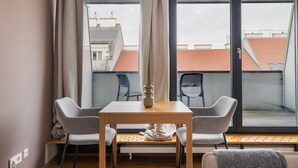 Une pièce moderne avec une table en bois et deux chaises grises, un vase blanc et une vue sur les bâtiments à travers de grandes fenêtres.