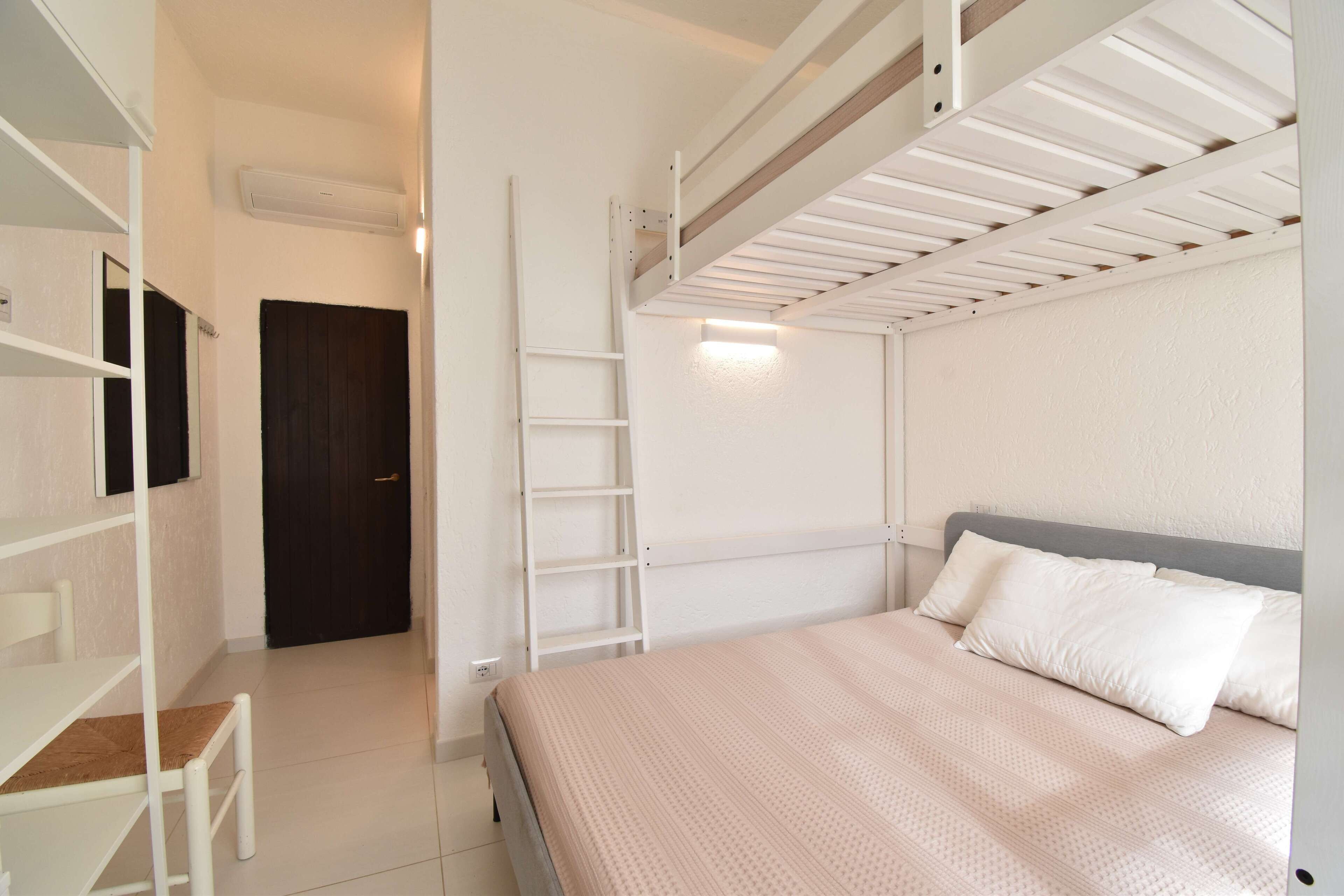 A bedroom with a bunk bed, a desk, and a ladder.