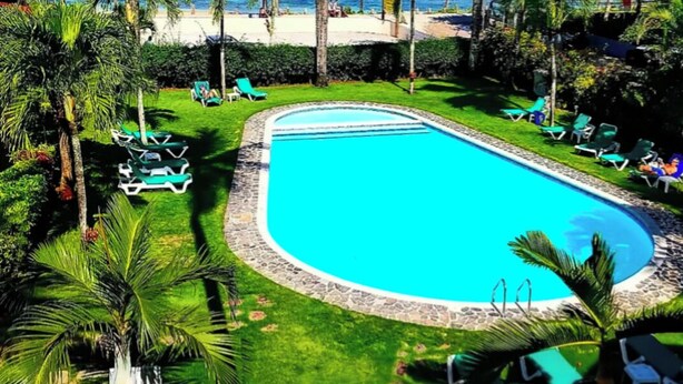 Ein Swimmingpool, umgeben von Palmen und Liegestühlen, mit Blick auf den Ozean.